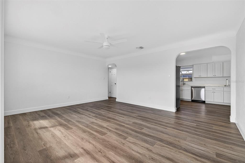 A spacious living room with wood-look flooring leads to an arched doorway into a kitchen — 211 89TH AVENUE N, ST PETERSBURG, FL