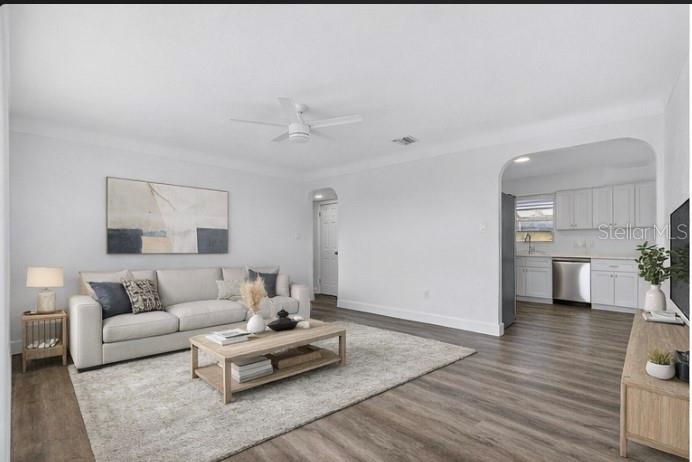 A living room with light wood flooring, a beige sofa, and an arched kitchen entrance — 211 89TH AVENUE N, ST PETERSBURG, FL