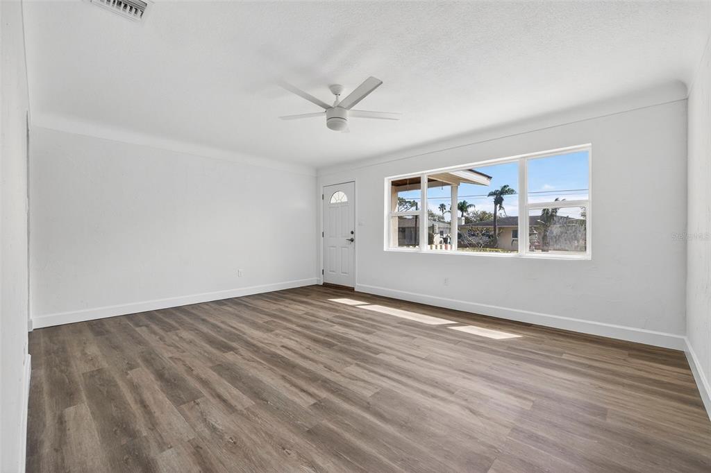 An empty room features white walls, wood-look flooring, a ceiling fan, and a large window — 211 89TH AVENUE N, ST PETERSBURG, FL
