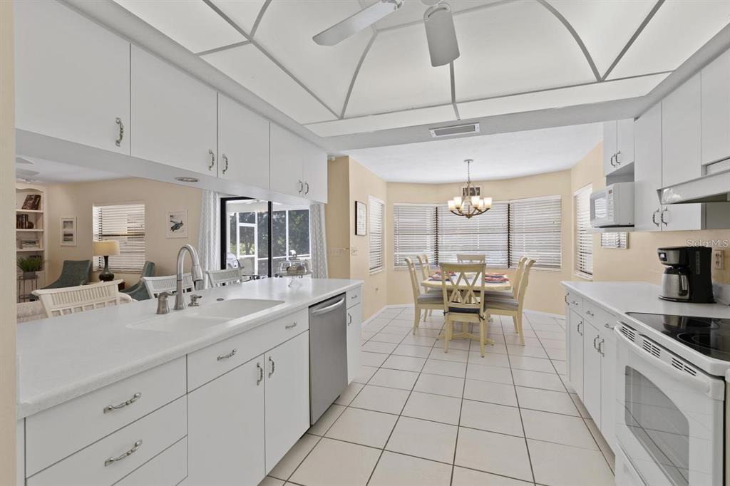 A bright kitchen with white cabinets and appliances opens to a dining area with windows — 1895 BUCCANEER CIRCLE, SARASOTA, FL