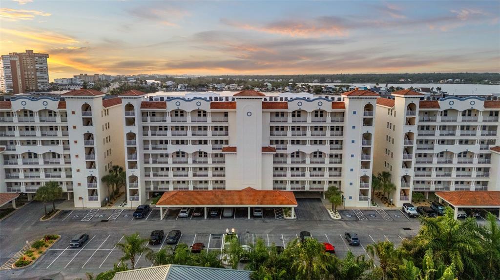 An aerial view shows a multi-story apartment building with a parking lot and sunset sky — 17717 GULF BOULEVARD UNIT 604, REDINGTON SHORES, FL