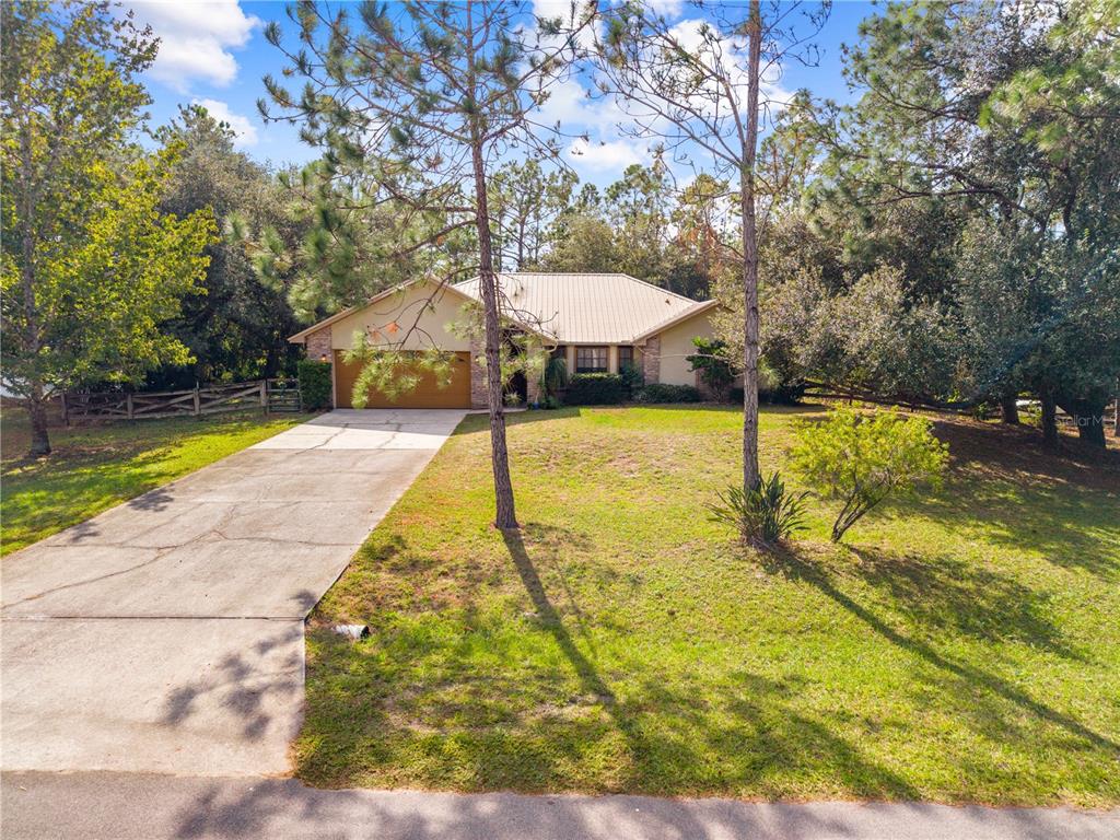 A single-story house with a metal roof and a concrete driveway sits on a lawn — 1860 MUSTANG COURT, ST CLOUD, FL