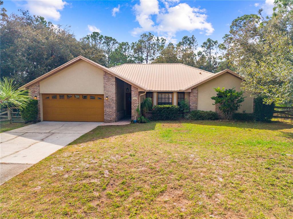 A single-story house with a metal roof, brick accents, and an attached two-car garage — 1860 MUSTANG COURT, ST CLOUD, FL