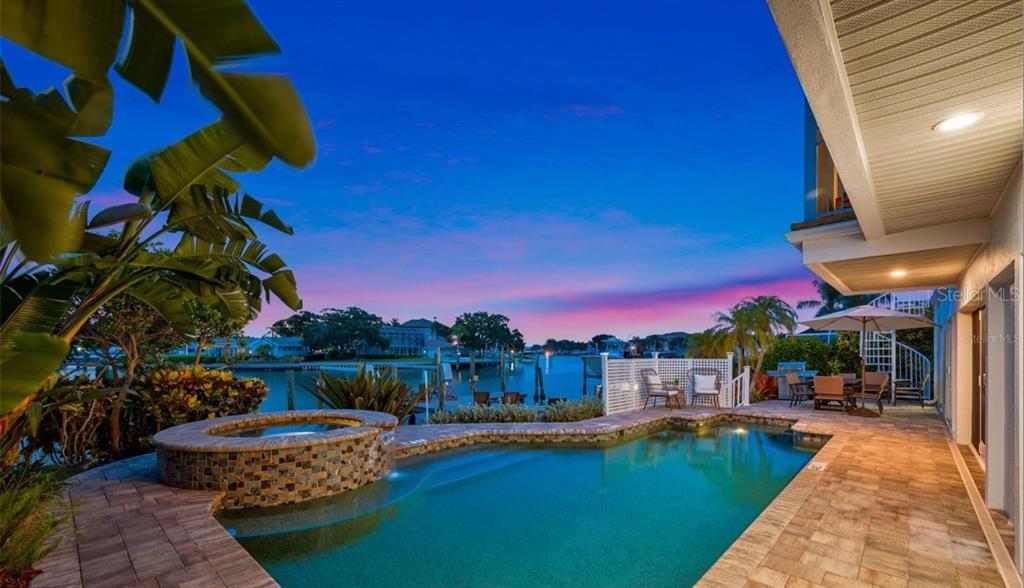 A swimming pool and hot tub overlook a canal at sunset from a paved patio — 4545 HARBOR HILLS DRIVE, LARGO, FL