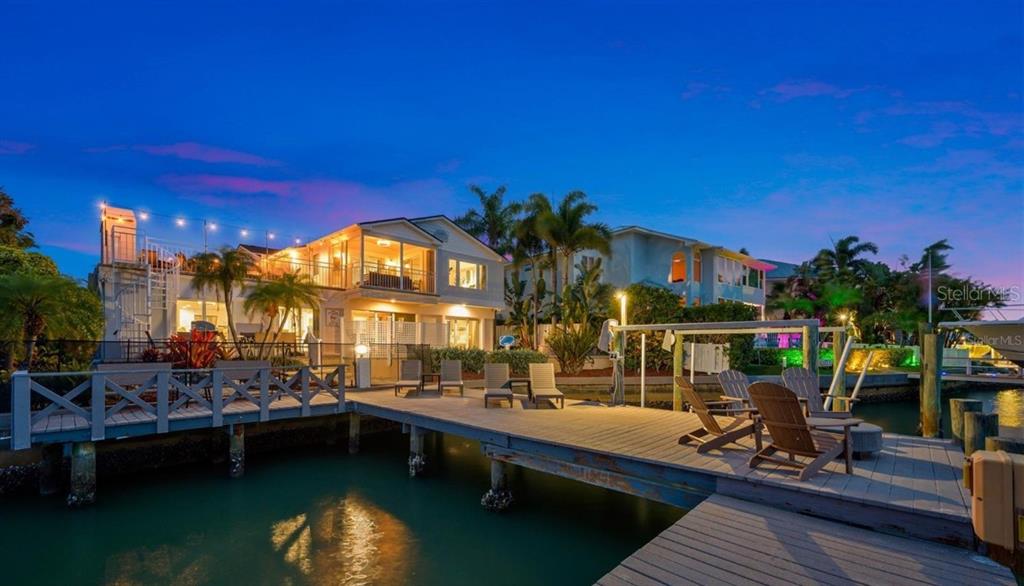 A waterfront house with a wooden dock, outdoor seating, and a spiral staircase at dusk — 4545 HARBOR HILLS DRIVE, LARGO, FL