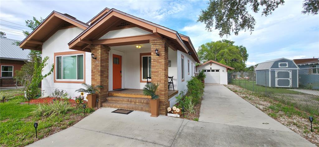A white bungalow with a brick-pillared porch, orange front door, and a detached garage — 107 S 1ST STREET, HAINES CITY, FL