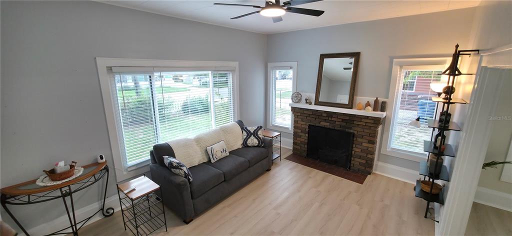 A living room features a brick fireplace, a gray sofa, and light wood-look flooring — 107 S 1ST STREET, HAINES CITY, FL