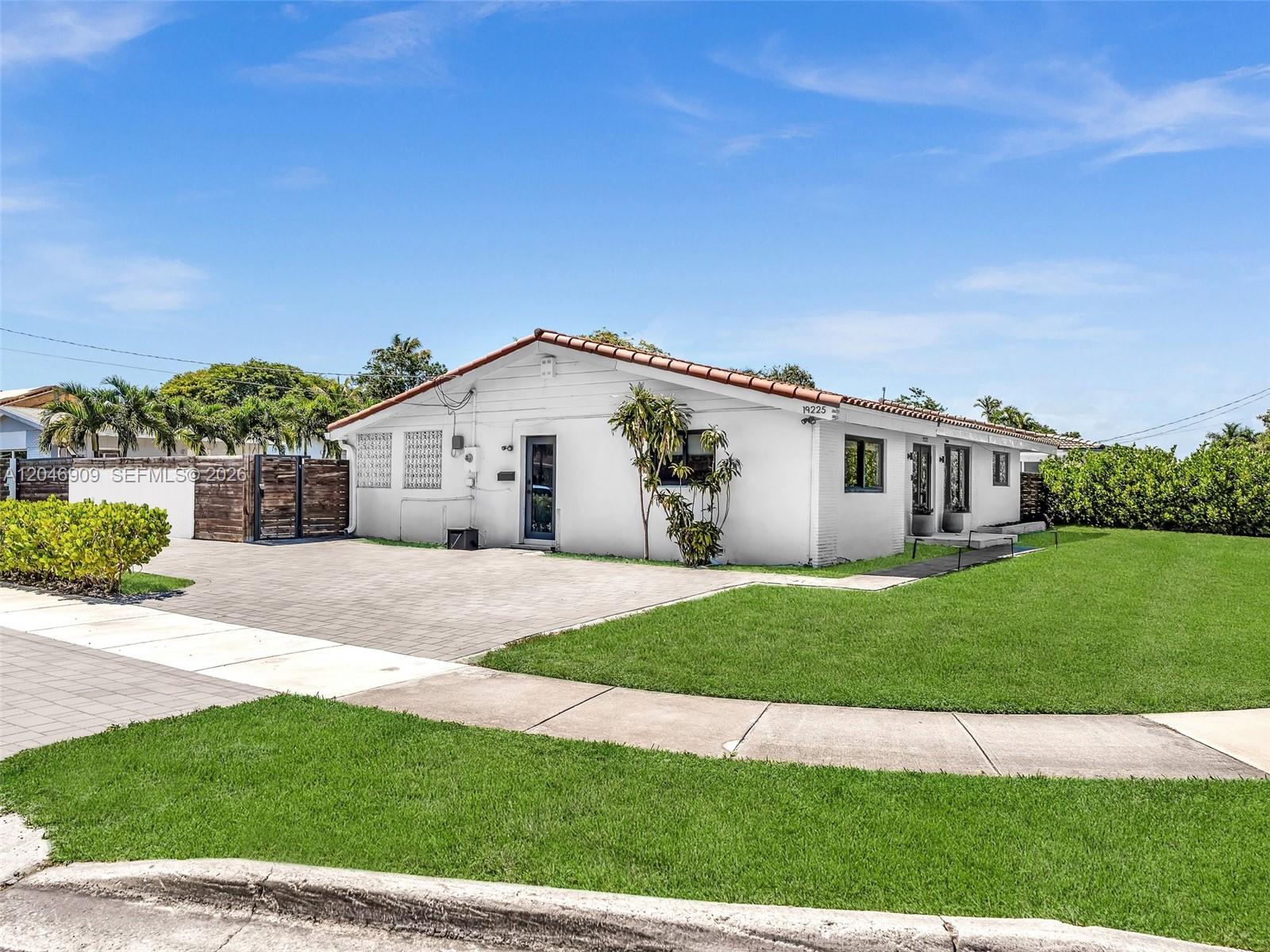A white single-story house with a tiled roof sits behind a paved driveway and lawn — 19225 NE 18th Ave, Miami FL 33179, MIAMI, FL