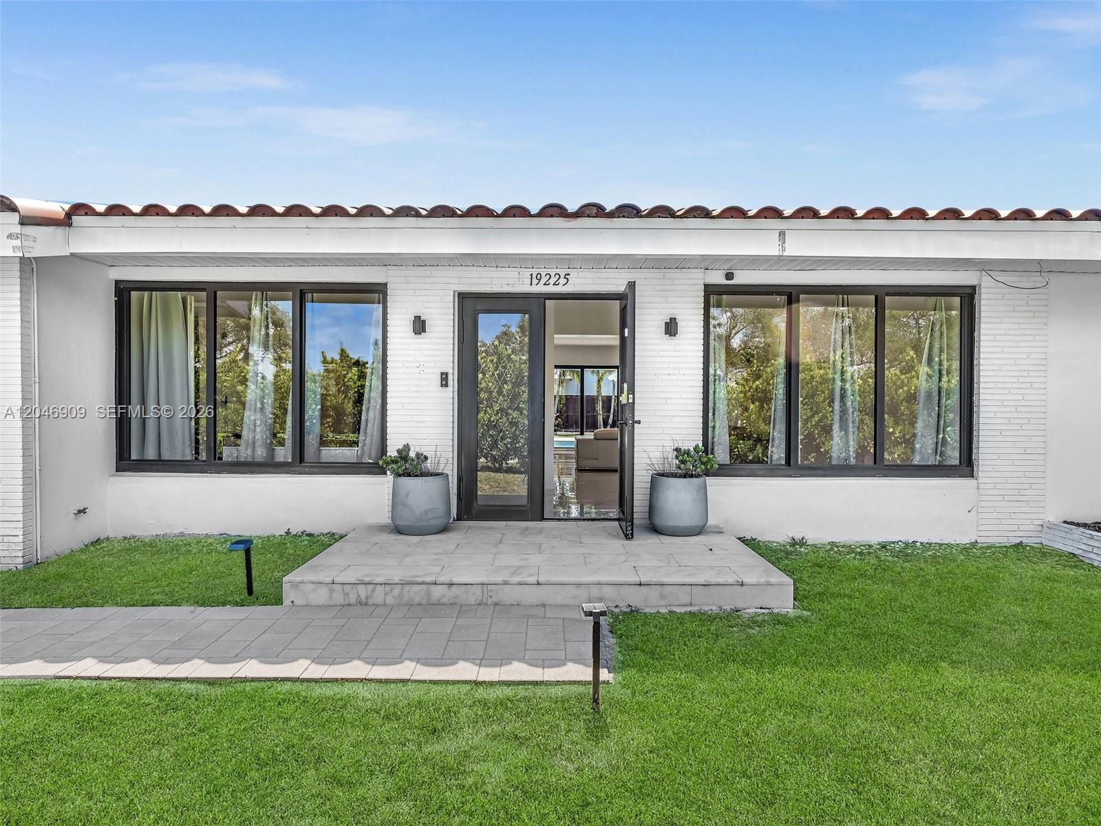 A white brick house features a tiled roof, large windows, and a central glass door — 19225 NE 18th Ave, Miami FL 33179, MIAMI, FL