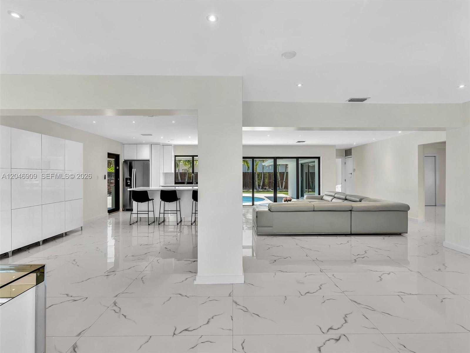 An open-concept living area features white marble-look tile floors, a modern kitchen, and a sectional sofa — 19225 NE 18th Ave, Miami FL 33179, MIAMI, FL