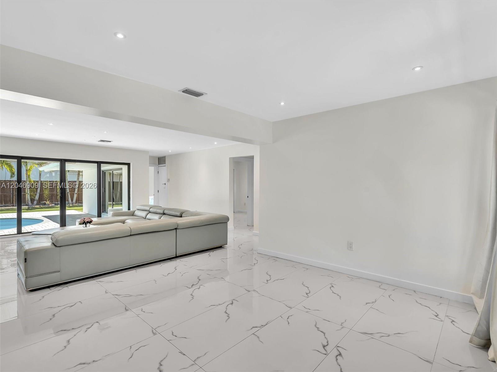 A living room features white marble-look tile floors, a large grey sectional, and sliding doors — 19225 NE 18th Ave, Miami FL 33179, MIAMI, FL