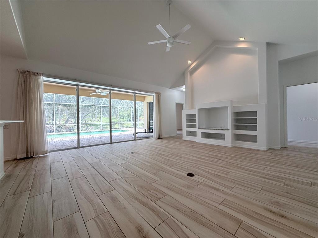 A spacious living room features light wood-look tile flooring, a vaulted ceiling, and built-in shelving — 4690 W TOMAHAWK DRIVE, BEVERLY HILLS, FL