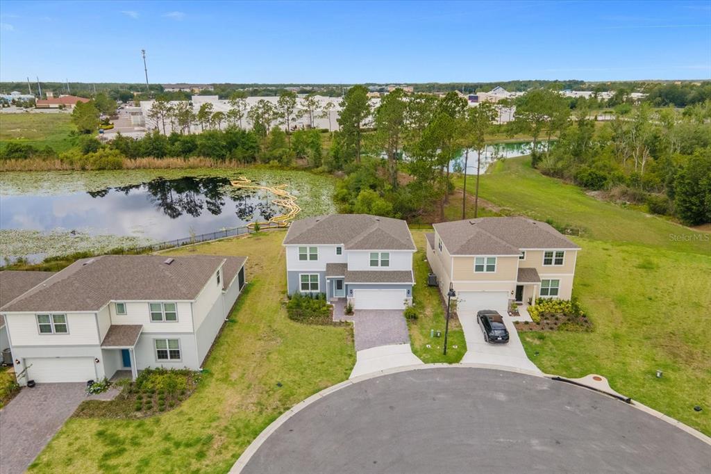 An aerial view shows three suburban houses situated near a pond and grassy area — 17315 MILLION LAKES COURT, CLERMONT, FL