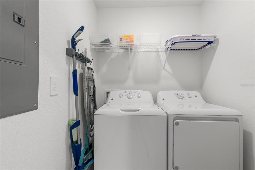 A laundry room features a white washer and dryer, a wire shelf, and wall-mounted cleaning tools — 17570 OPAL SAND DRIVE UNIT 201, VENICE, FL