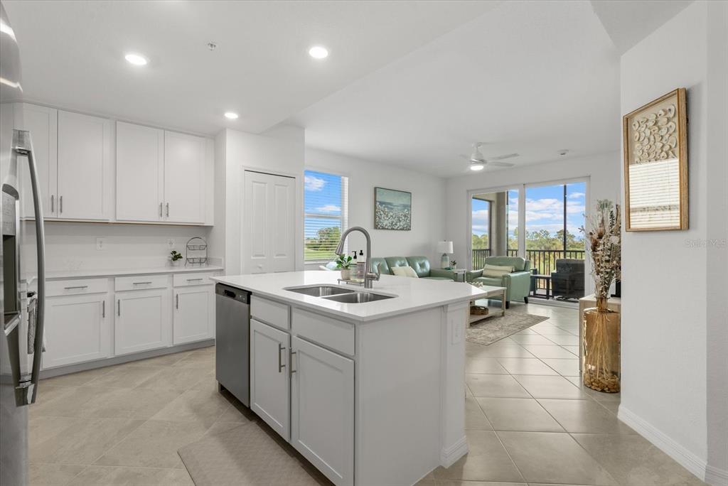 A modern kitchen with white cabinets and a central island opens into a living area — 17570 OPAL SAND DRIVE UNIT 201, VENICE, FL