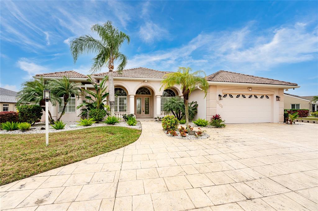 A single-story house with a tiled roof, beige stucco exterior, and a paved driveway — 12109 SW KINGSWAY CIRCLE, LAKE SUZY, FL