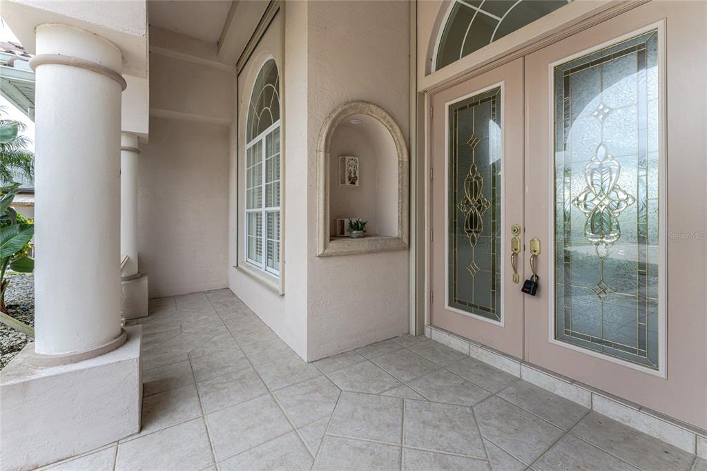 A covered entryway features a tiled floor, double glass-paneled doors, and a decorative wall niche — 12109 SW KINGSWAY CIRCLE, LAKE SUZY, FL