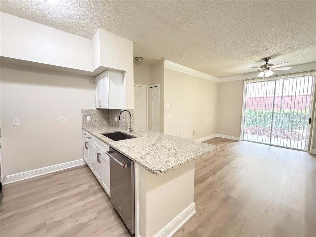 A kitchen with granite countertops and white cabinets opens to a living area with flooring — 13015 PLANTATION PARK CIRCLE UNIT 10111, ORLANDO, FL