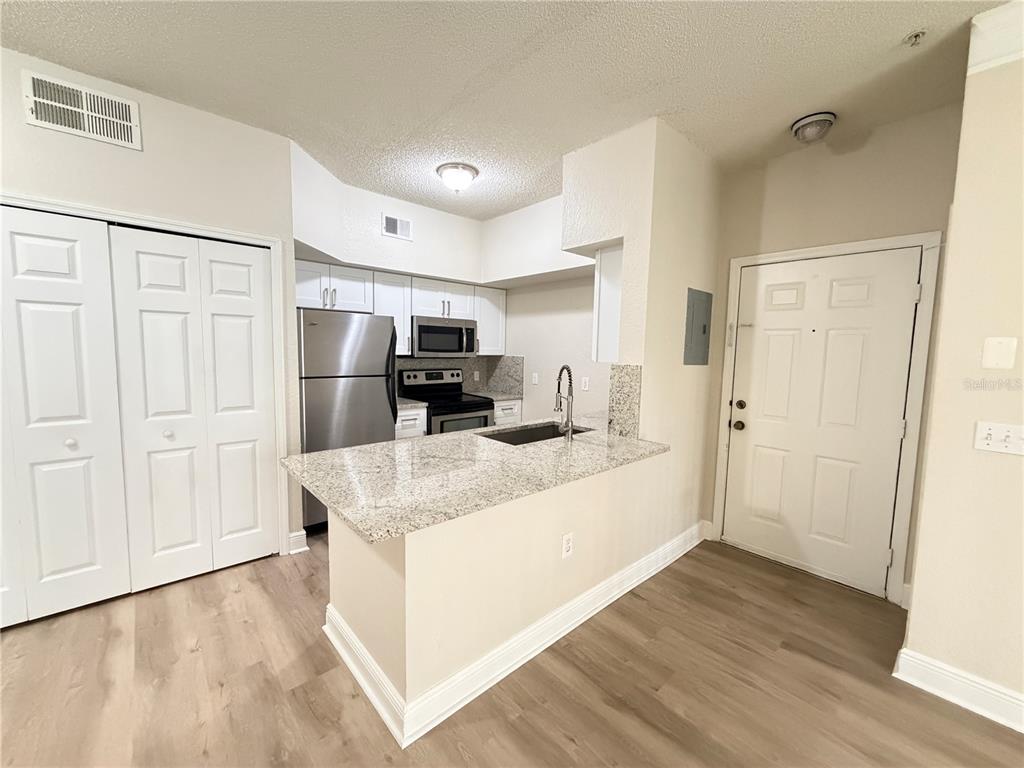 A kitchen features a granite breakfast bar, stainless steel appliances, and light wood-look flooring — 13015 PLANTATION PARK CIRCLE UNIT 10111, ORLANDO, FL