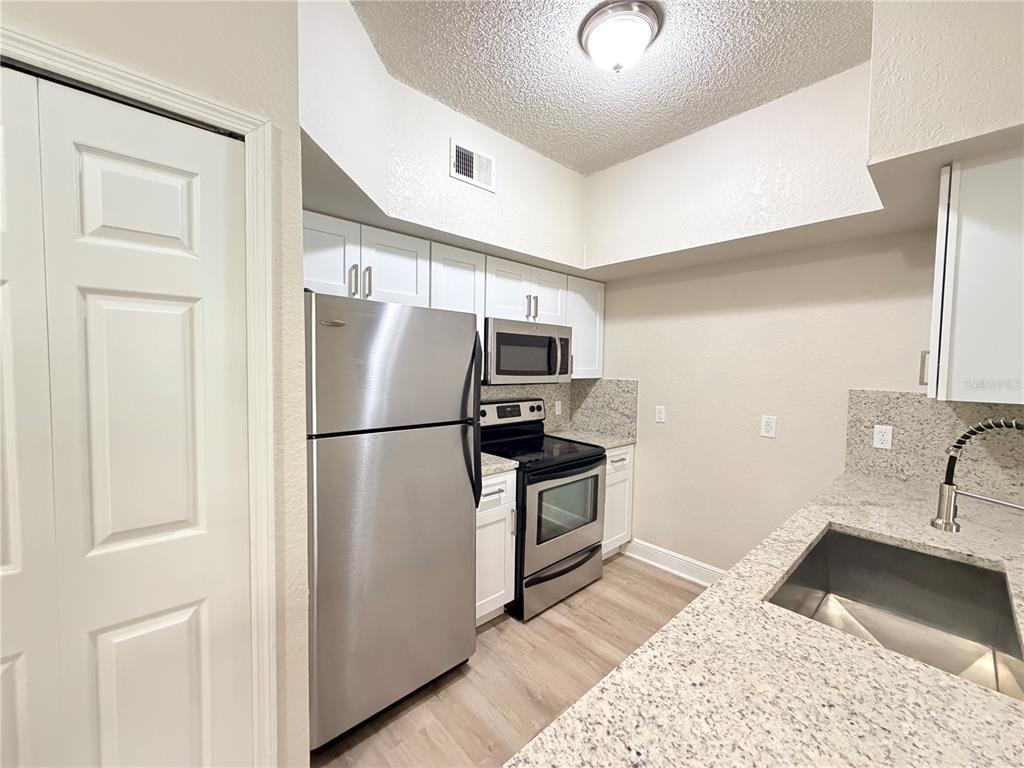 A kitchen features stainless steel appliances, white cabinets, and granite countertops — 13015 PLANTATION PARK CIRCLE UNIT 10111, ORLANDO, FL