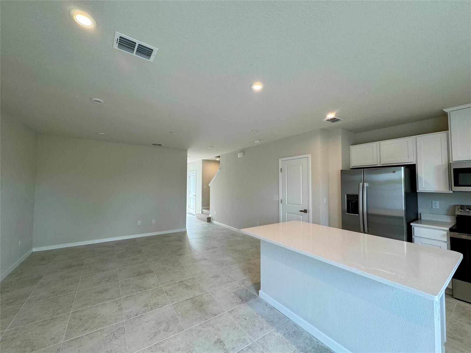 An open-concept kitchen and living area features tile flooring, white cabinetry, and stainless steel appliances — PORT ST. LUCIE, FL