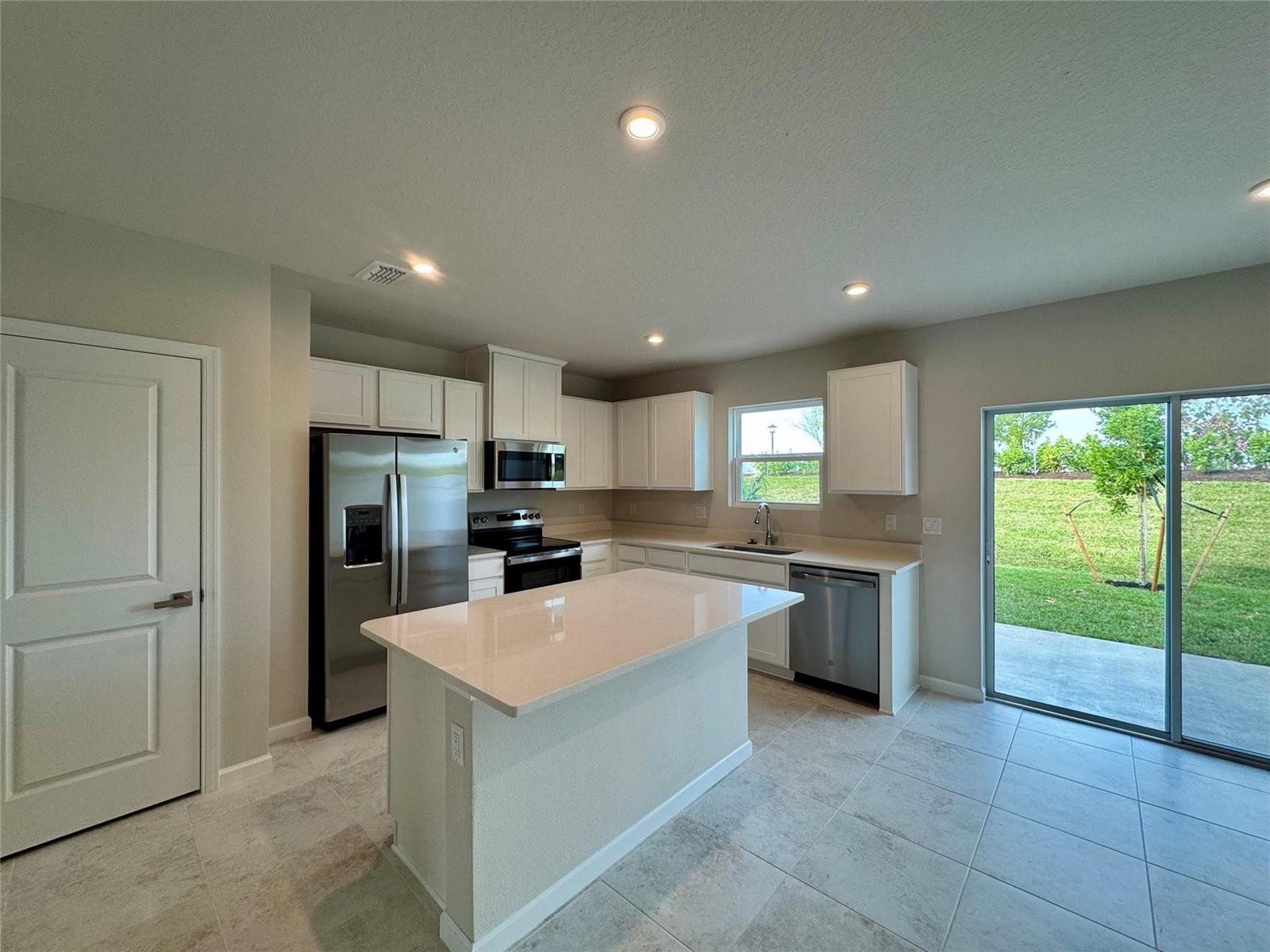 A modern kitchen features white cabinets, stainless steel appliances, a quartz island, and tile flooring — PORT ST. LUCIE, FL
