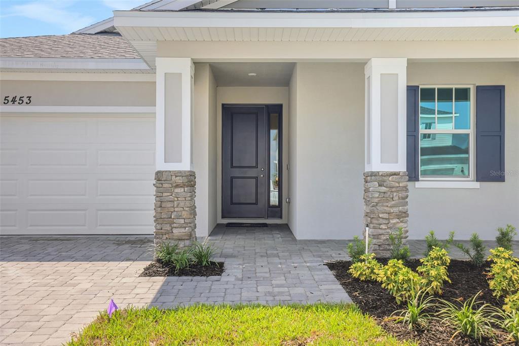 The exterior of a house features a stone-accented porch, a dark front door, and a garage — 5453 NW CAMBERLY COURT, PORT ST LUCIE, FL