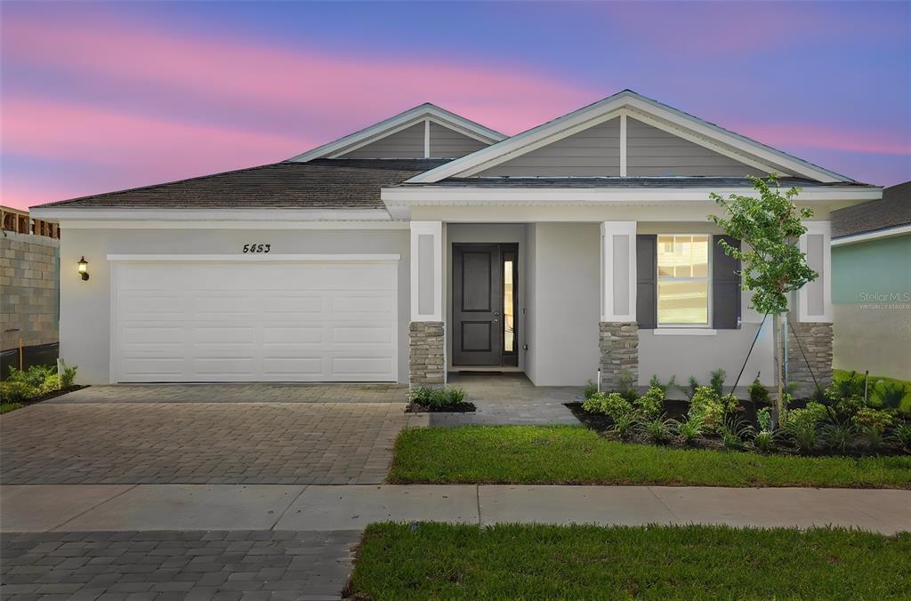 A single-story house with a gray exterior, stone accents, and a paved driveway at sunset — 5453 NW CAMBERLY COURT, PORT ST LUCIE, FL