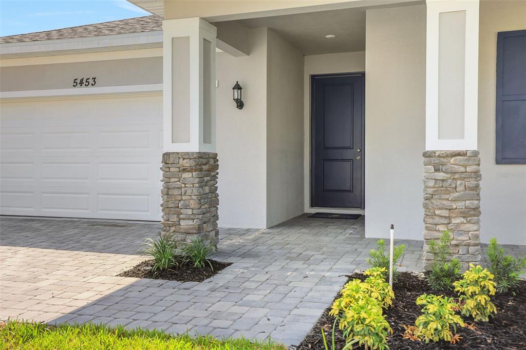 The exterior of a house features a stone-based pillar, a dark door, and a paver walkway — 5453 NW CAMBERLY COURT, PORT ST LUCIE, FL