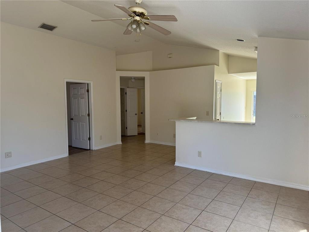 A living room with beige tile flooring, a ceiling fan, and a kitchen pass-through window — 11106 HAVASU COURT, RIVERVIEW, FL