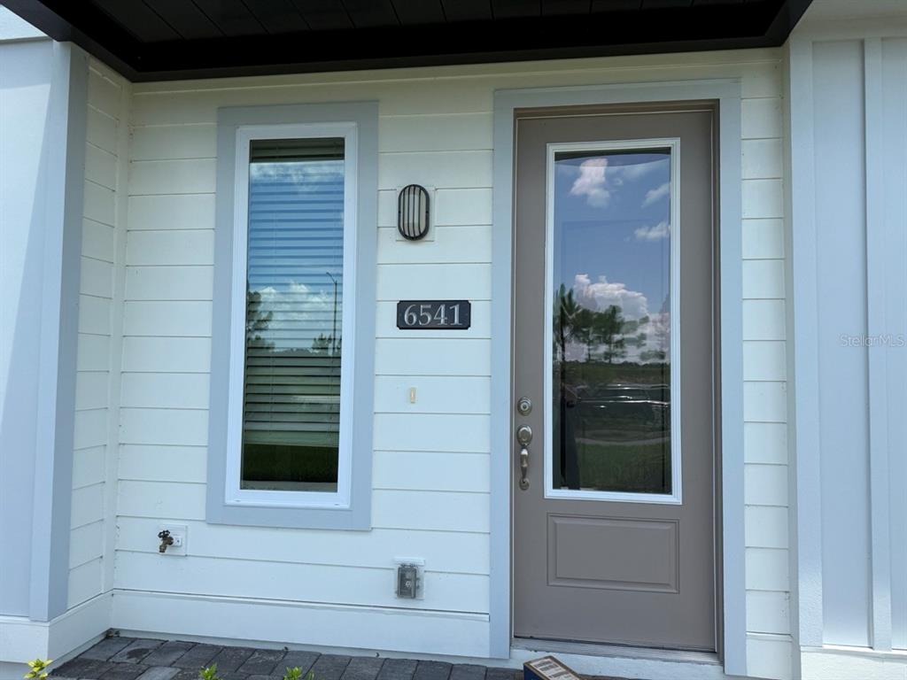 The exterior of a home features white horizontal siding, a gray front door, and a window — 6541 CYRILS DRIVE, ST CLOUD, FL