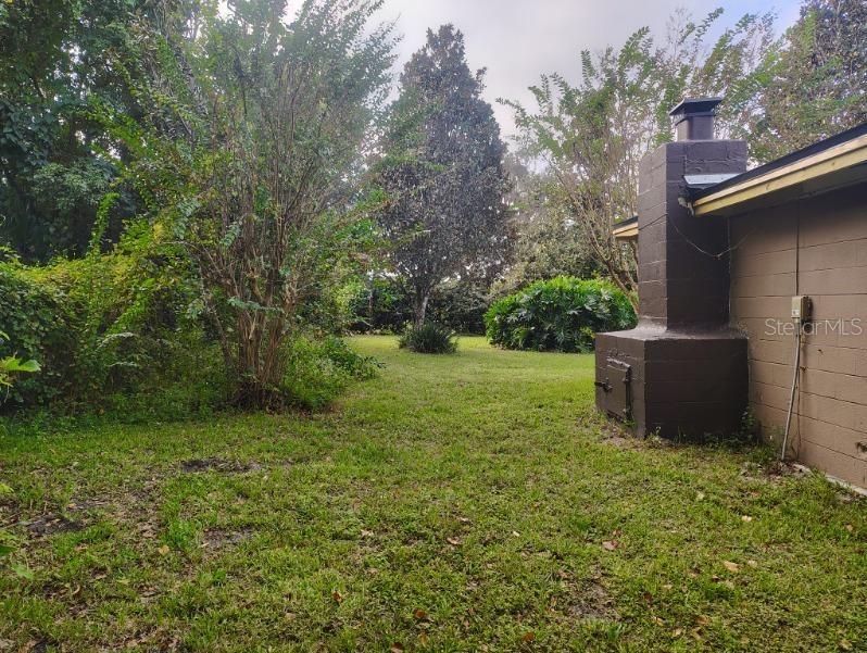 A backyard view showing a brown concrete block chimney attached to the side of a house — 20621 SE HIGHWAY 42, UMATILLA, FL
