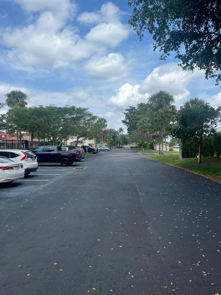 A paved parking lot with parked vehicles is surrounded by trees and residential buildings — 9993 Three Lakes Circle, Boca Raton FL 33428, BOCA RATON, FL
