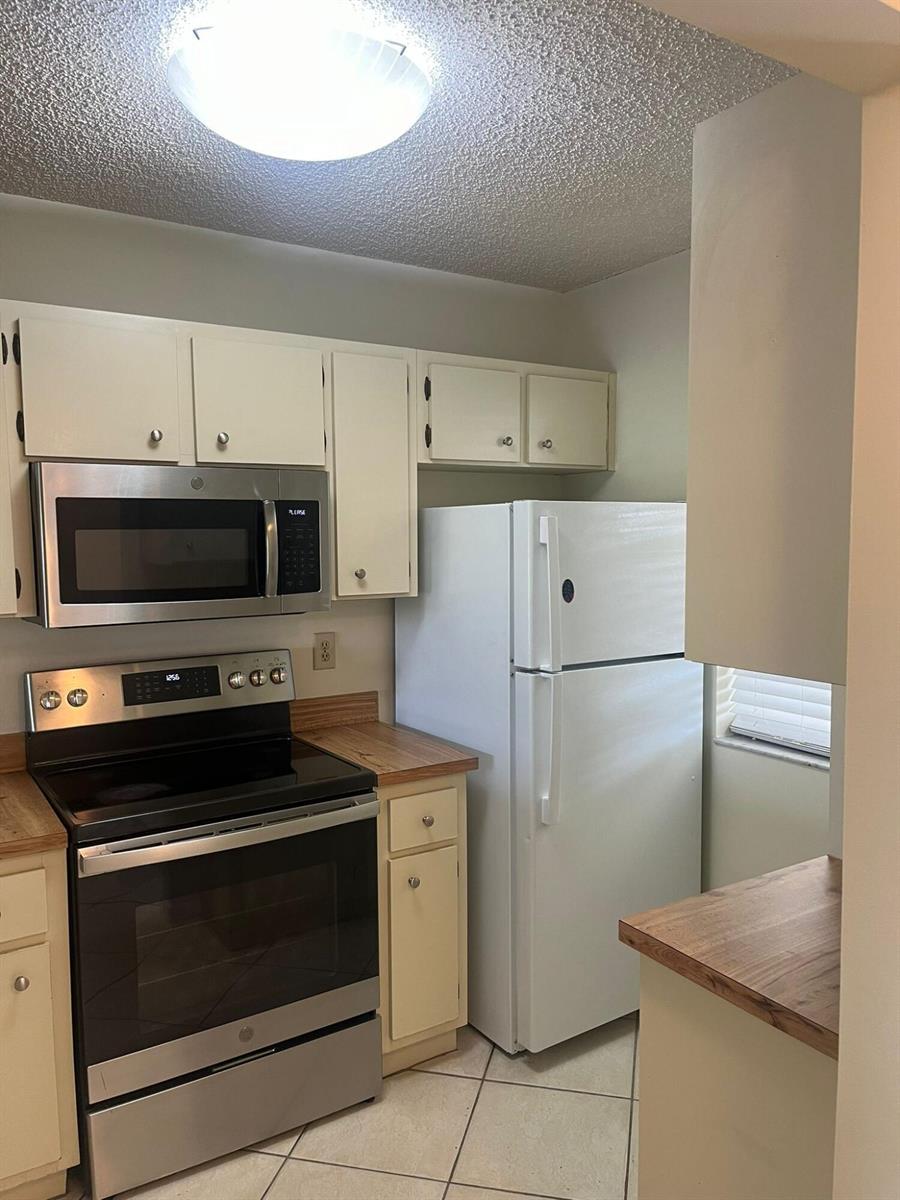A kitchen features white cabinets, stainless steel appliances, a white refrigerator, and wood-look countertops — 9993 Three Lakes Circle, Boca Raton FL 33428, BOCA RATON, FL
