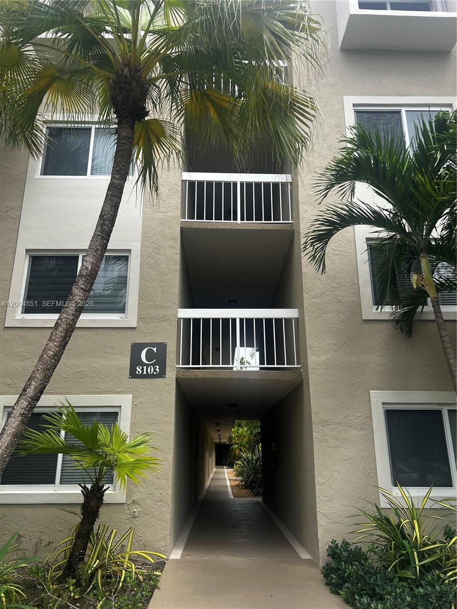 A multi-story apartment building exterior features a central walkway, white railings, and palm trees — 8103 Camino Real # 407, Miami FL 33143, MIAMI, FL