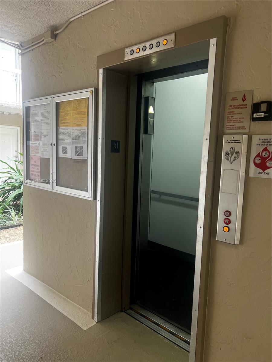 An elevator with a metal control panel and a nearby bulletin board in a hallway — 8103 Camino Real # 407, Miami FL 33143, MIAMI, FL