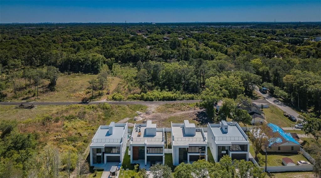 An aerial view shows four modern, flat-roofed townhouses situated next to a wooded area — 310 SKYTRAIL, TAMPA, FL