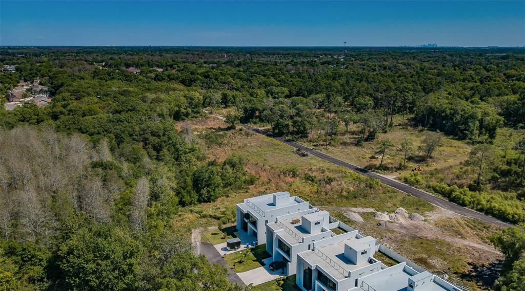 An aerial view shows a modern white multi-unit building next to a road and forest — 310 SKYTRAIL, TAMPA, FL