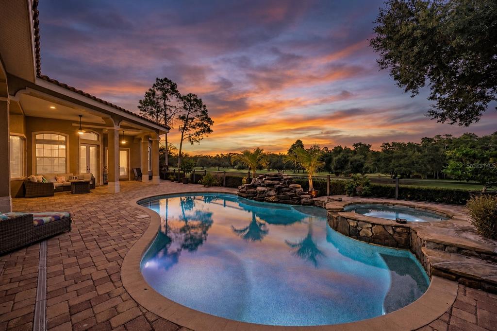 A backyard patio features a swimming pool, a stone hot tub, and a sunset view — 1306 PLAYMOOR DRIVE, PALM HARBOR, FL