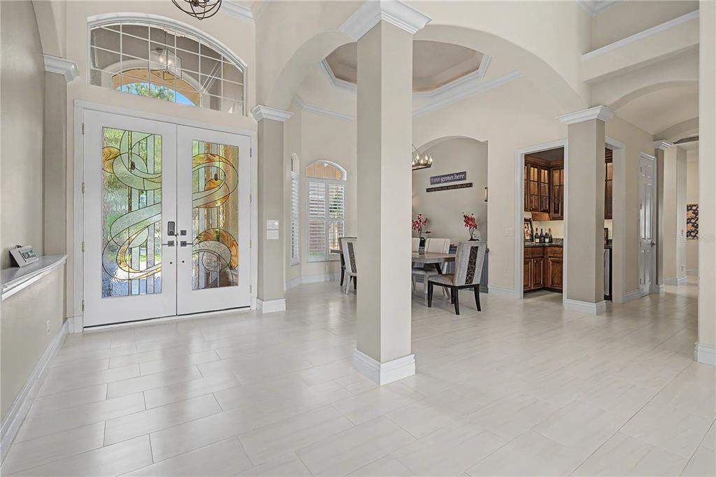 A bright foyer with white tile floors, arched architectural details, and double glass-paneled entry doors — 1306 PLAYMOOR DRIVE, PALM HARBOR, FL
