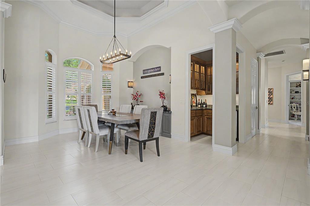 A dining room with a tray ceiling, chandelier, light tile floors, and an adjacent butler's pantry — 1306 PLAYMOOR DRIVE, PALM HARBOR, FL