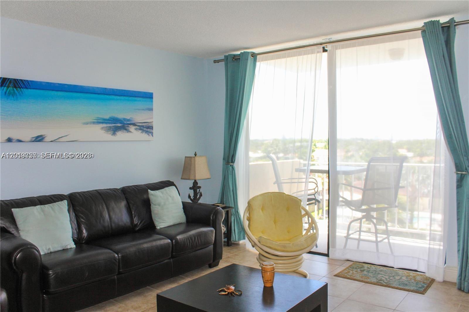 A living room features a black leather sofa, a yellow chair, and a balcony view — 2350 NE 135th St # 507, North Miami FL 33181, NORTH MIAMI, FL