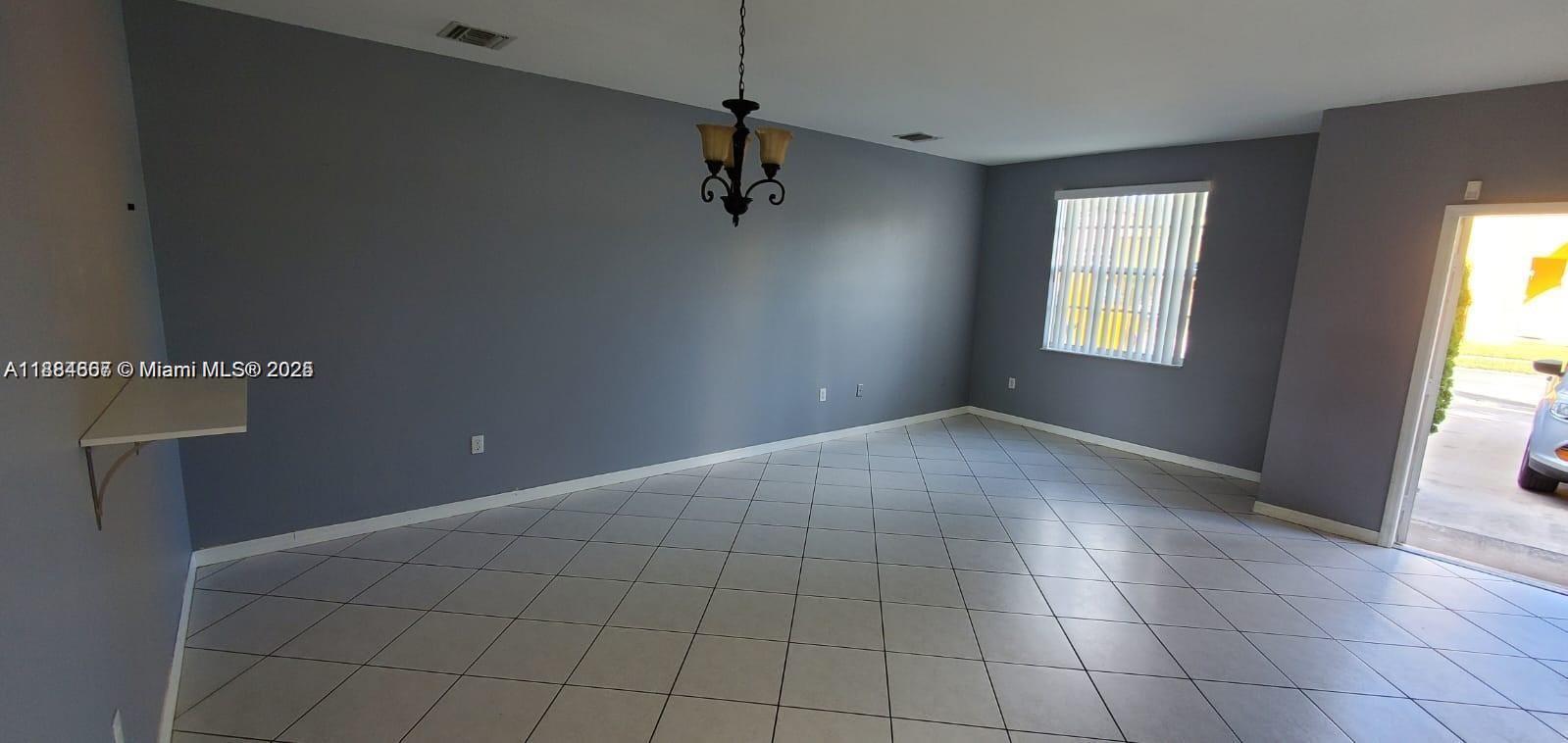An empty room with gray walls, white tile flooring, a chandelier, and a window — 60 SE 6th Rd, Homestead FL 33030, HOMESTEAD, FL