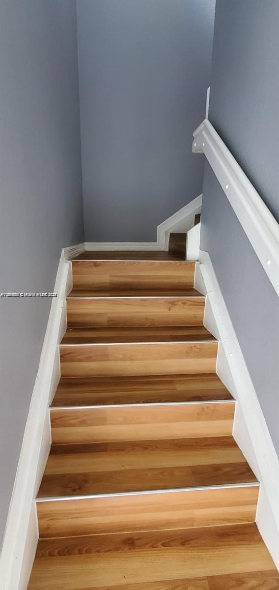 A staircase with wood-look flooring, white trim, and a white handrail against gray walls — 60 SE 6th Rd, Homestead FL 33030, HOMESTEAD, FL