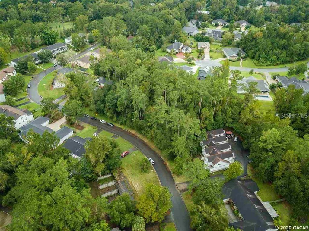 An aerial view shows a suburban neighborhood with houses nestled among dense trees and roads — 2730 NW 104TH COURT, GAINESVILLE, FL