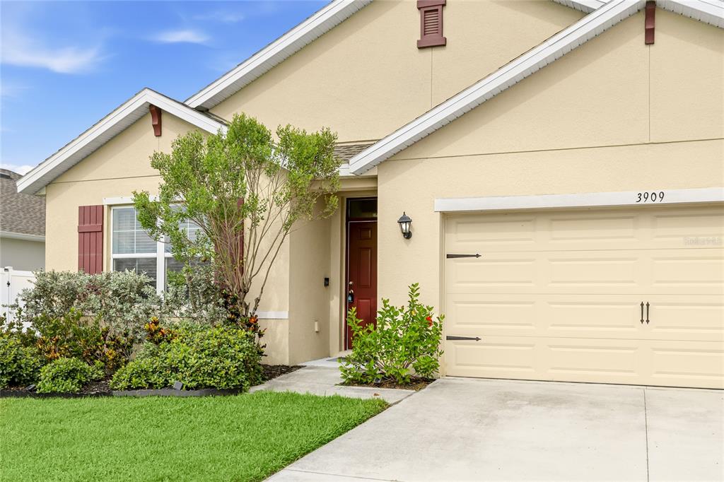 The exterior of a single-story house features a tan stucco facade, a garage, and landscaping — 3909 PARK WILLOW AVENUE, PALMETTO, FL