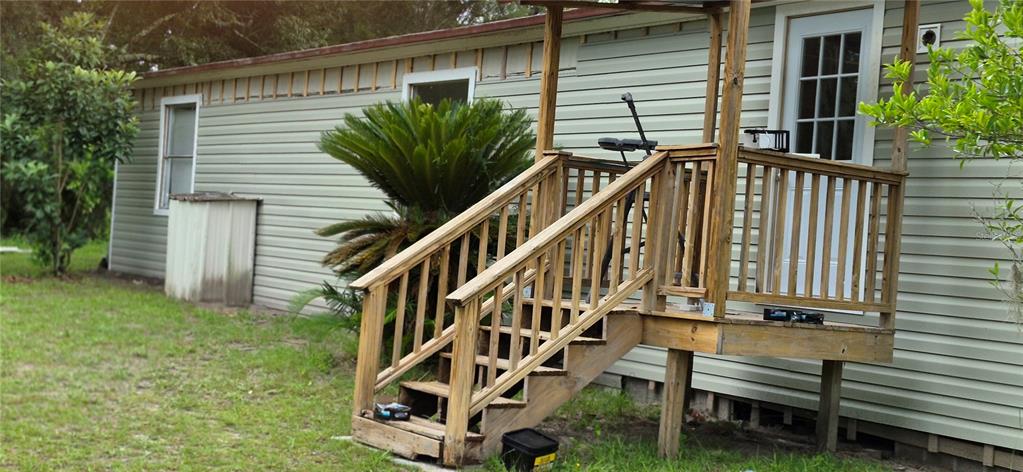 A light green mobile home exterior features a wooden porch with stairs and a palm plant — 17416 NW 89TH TERRACE, FANNING SPRINGS, FL
