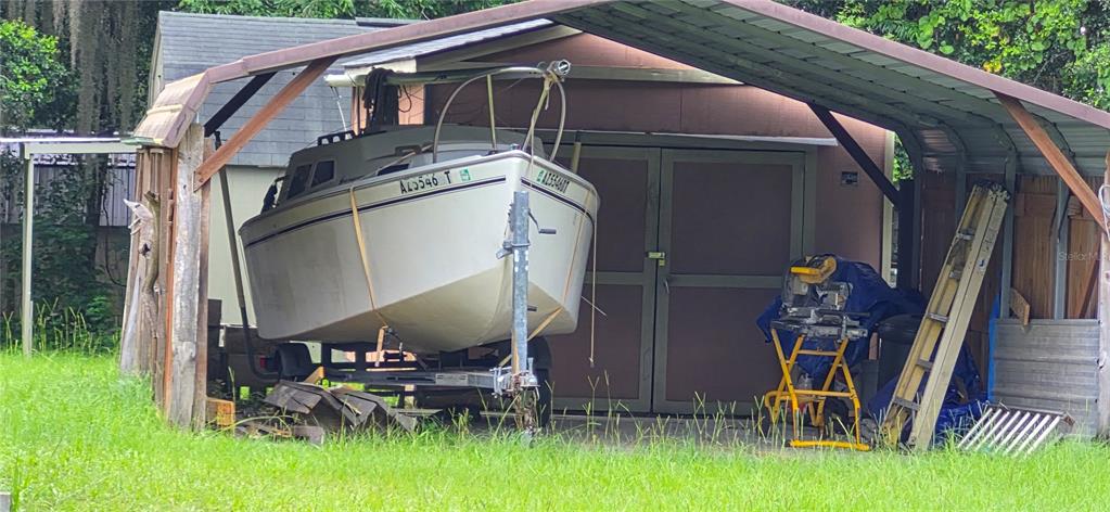 A sailboat on a trailer is parked under a metal carport next to a shed — 17416 NW 89TH TERRACE, FANNING SPRINGS, FL