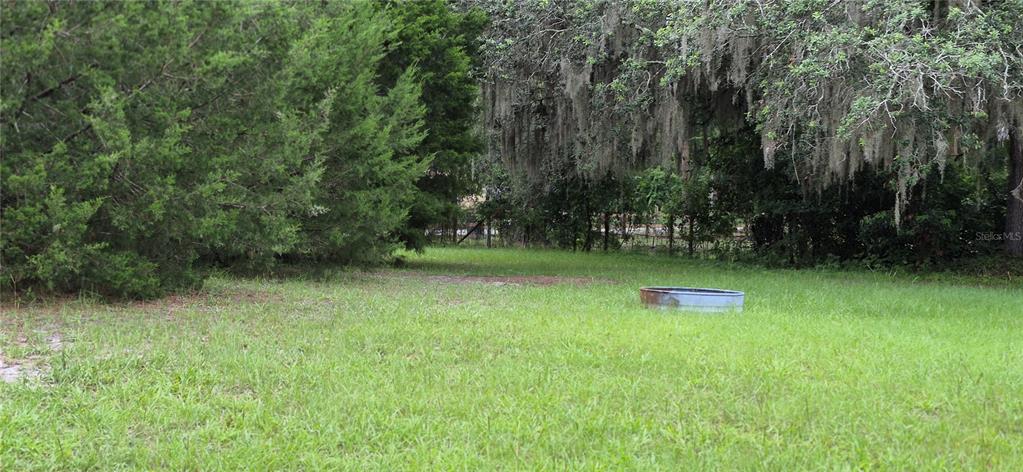 A grassy, partially shaded lot features a metal stock tank in the foreground — 17416 NW 89TH TERRACE, FANNING SPRINGS, FL