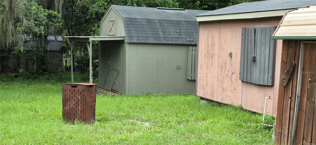 Three storage sheds sit in a grassy yard with a metal trash bin in front — 17416 NW 89TH TERRACE, FANNING SPRINGS, FL